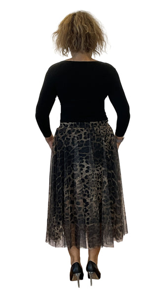 Person wearing a black top and leopard print skirt standing against a white wall.
