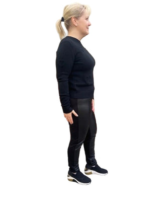 Woman wearing a black outfit standing against a brick wall.