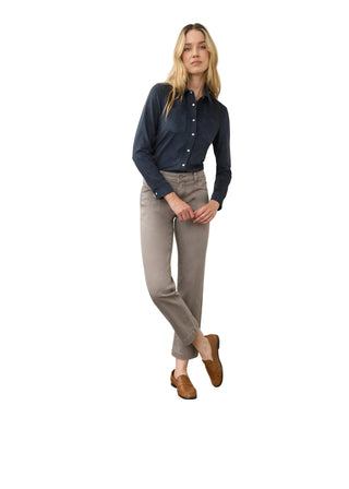 A woman modeling a dark navy long-sleeve button-down shirt, light gray slim-fit pants, and brown suede loafers, standing against a plain off-white wall and concrete floor.