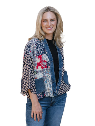Woman wearing a patchwork denim jacket against a textured wall.