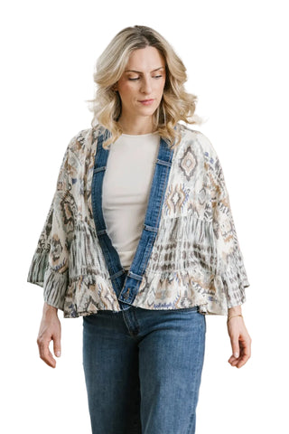 Woman wearing a patterned jacket over a white shirt and blue jeans in a room with a radiator and wooden cabinet.