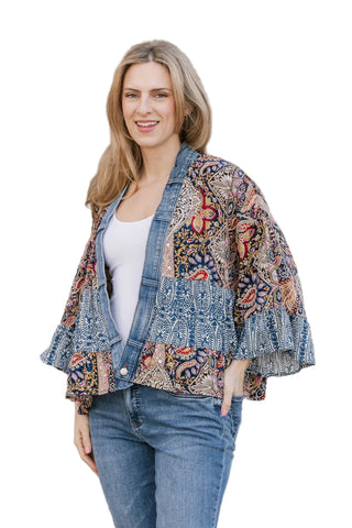 Woman wearing a floral kimono jacket over a denim jacket against a stone wall.
