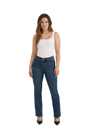 A woman modeling a pair of dark blue straight-leg jeans with a white tank top and black heels, standing against a light gray studio background.