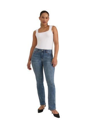 A woman modeling a pair of medium-wash blue skinny jeans with a white tank top and black pointed-toe heels, standing against a neutral light gray studio background.