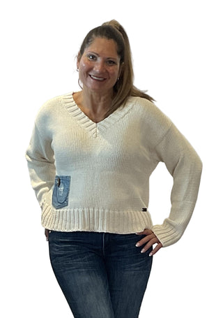 Woman wearing a cream sweater with a denim pocket against a plain background