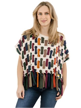 Woman wearing a colorful patterned top with tassels on a plain background