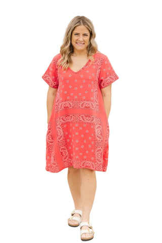 Woman wearing a red dress with white patterns standing against a stone wall.