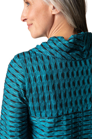 Close-up of a person wearing a teal patterned top against a beige background