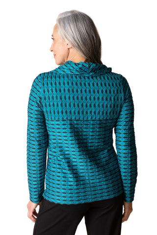 A woman with gray hair is shown from the back wearing a teal and black patterned hooded long-sleeve top against a solid beige background.