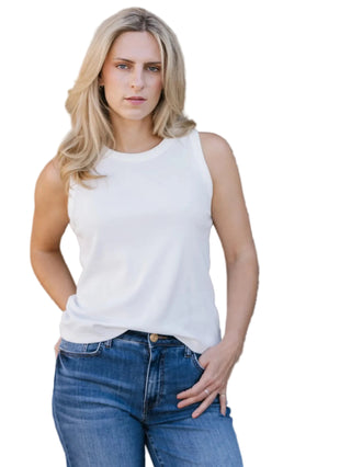 Woman wearing a white sleeveless top and blue jeans against a stone wall.