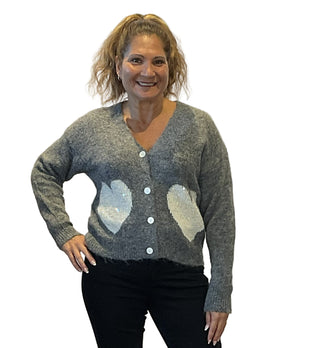 Woman wearing a gray cardigan with heart patterns on a plain background