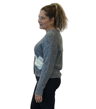 Woman wearing a gray sweater with a shiny panel on a plain background