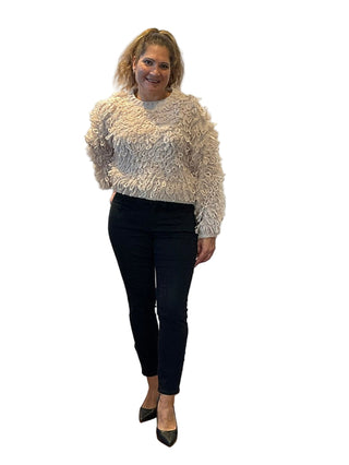 Woman in a textured sweater and black pants standing in front of an 'Anne's on the Avenue' backdrop.