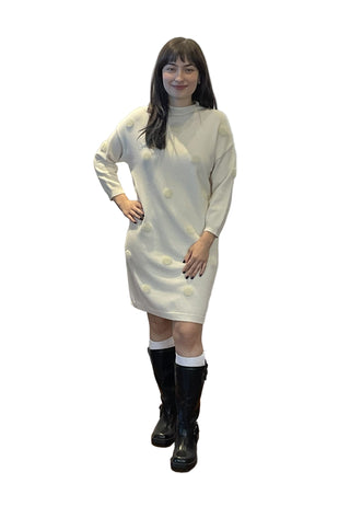 Person wearing a white dress with buttons and black boots standing in front of an 'ANN' branded backdrop.
