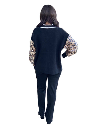 Person wearing a black sweater with leopard print sleeves in front of a building entrance.