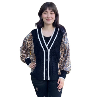 Woman wearing a black cardigan with white trim standing in front of a brick building.