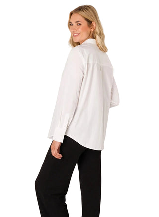 Woman wearing a white blouse and black pants against a plain background