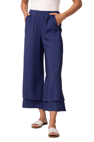 Person wearing blue wide-leg pants and white sandals on a light wooden floor with a white wall background