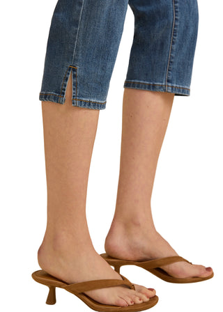 Brown sandals worn with rolled-up blue jeans on a beige background