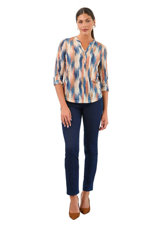 Woman wearing a patterned blouse and blue jeans against a white background