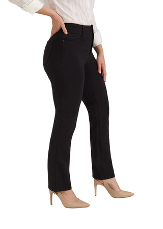 A model wearing black slim-fit trousers, styled with a white long-sleeve blouse and beige high-heeled pumps, shown from the waist down against a light gray studio background.
