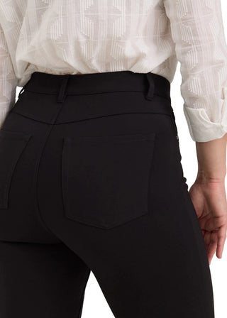 Close-up back view of a person wearing black high-waisted riding pants with a structured waistband and back pocket, paired with a white patterned blouse.