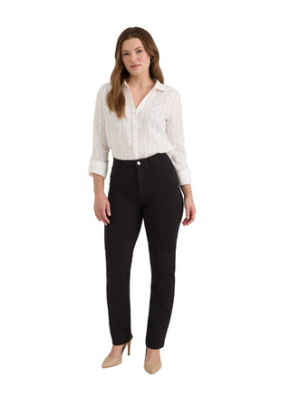 A woman modeling black slim-fit trousers with a white striped button-down shirt and beige heels, standing against a light gray studio background.