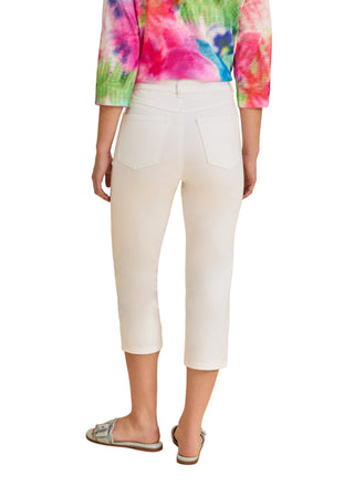 Person wearing white capri pants with a colorful tie-dye shirt on a beige background