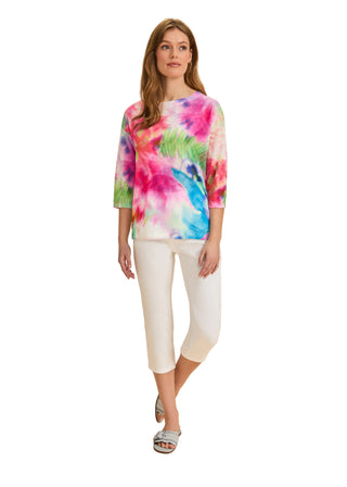 Woman wearing a colorful tie-dye shirt and white pants on a beige background