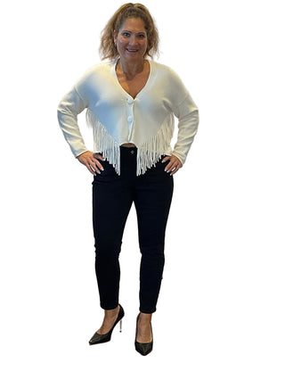 Woman wearing a white blouse with fringe and black pants standing in front of an 'Anne's on the Avenue' sign.