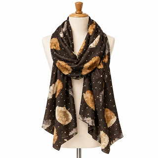 A black scarf with abstract tan, brown, and gray circular patterns and small white dots, draped on a white mannequin torso over a gray countertop.