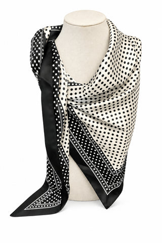 A black and white patterned scarf draped on a cream mannequin torso, set against a gray tiled floor and a light gray wall.