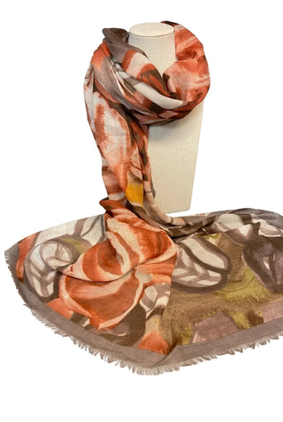 A lightweight scarf with an abstract floral pattern in orange, brown, beige, and olive green, draped over a white mannequin stand on a dark gray countertop.