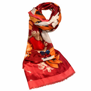 A lightweight scarf with a vibrant abstract floral pattern in red, orange, pink, and white, draped on a white mannequin torso over a gray tabletop.