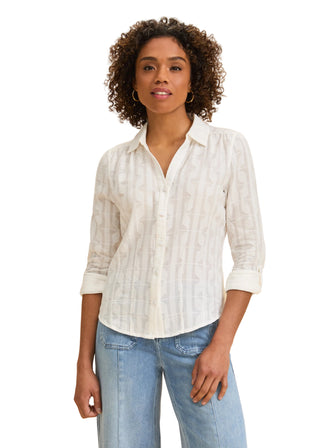 Woman wearing a white button-up shirt and light blue jeans against a beige background