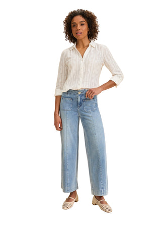 Woman wearing a white button-up shirt and blue jeans on a beige background