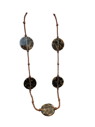 A beaded necklace with four large oval dark brown and black marbled stone pendants and a matching oval pendant at the center, displayed on a cream fabric mannequin bust against a gray tabletop and white wall.