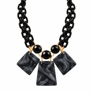 A black statement necklace displayed on a white mannequin bust, featuring a black chain and large faceted black stone-like geometric pendants.