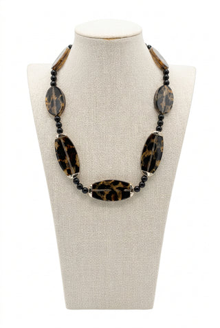 A statement necklace with large leopard-print oval beads and small black spacer beads, displayed on a cream fabric mannequin bust.