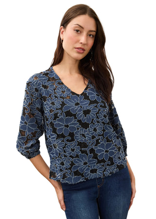 A woman modeling a blue and black floral lace blouse with three-quarter sleeves and a V-neckline, paired with dark blue jeans against a plain light background.