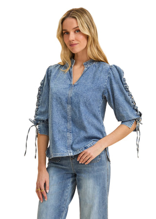 Woman wearing a denim blouse with ruffled sleeves on a beige background