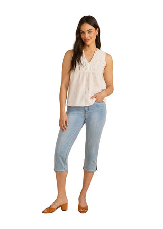 Woman wearing a white sleeveless top and blue jeans on a beige background