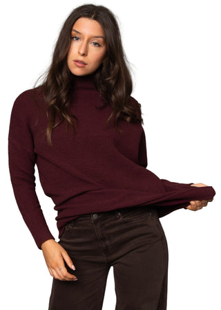 Woman wearing a burgundy turtleneck sweater against a gray background