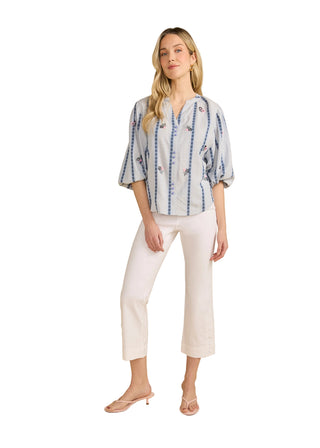 Woman wearing a blue and white patterned shirt with white pants on a beige background