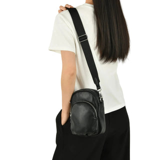 Person wearing a black leather crossbody bag on a plain background