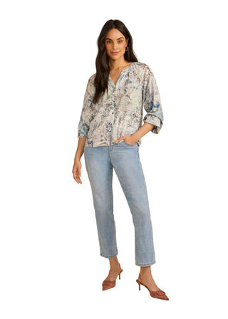 Woman wearing a floral blouse and light blue jeans on a beige background