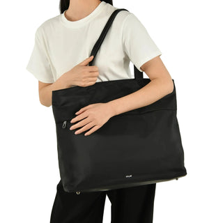 Person holding a black tote bag against a plain background