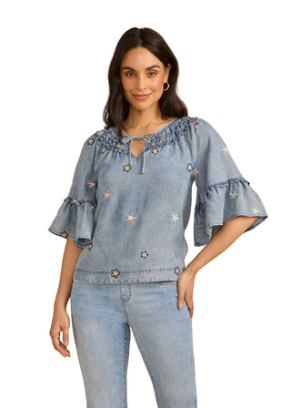 Woman wearing a denim blouse with floral embroidery on a beige background