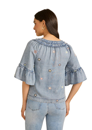 Woman wearing a denim outfit with floral embroidery on a beige background