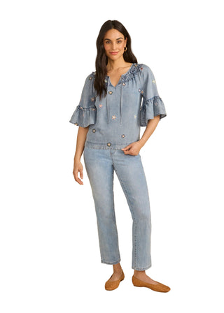 Woman wearing a denim outfit with a ruffled top and jeans on a beige background